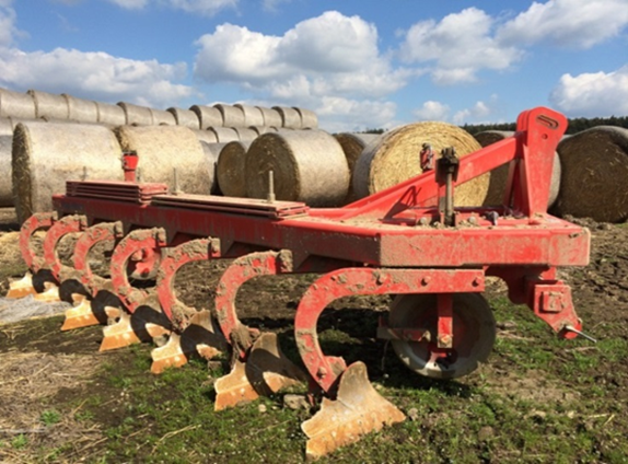 Ein roter Stoppelhobel mit Heuballen im Hintergrund